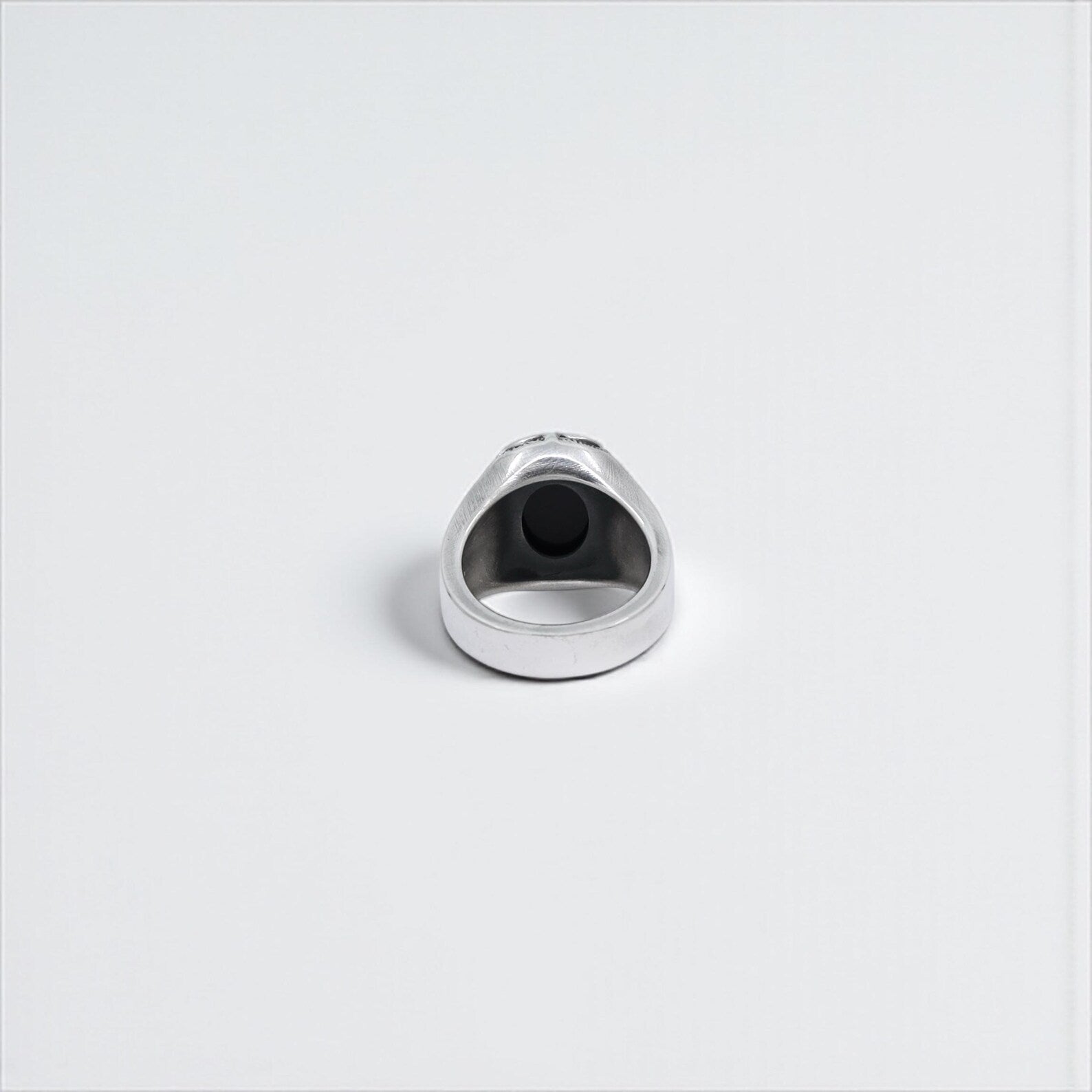 Flat-lay top view of a handcrafted sterling silver ring with a dominant black onyx stone, elaborate scroll motifs, and cross-inspired details on each side of the band—an exceptional piece of gothic men's jewelry, ideal as a birthday, anniversary, or Valentine's Day gift for a man with strong and unique style.