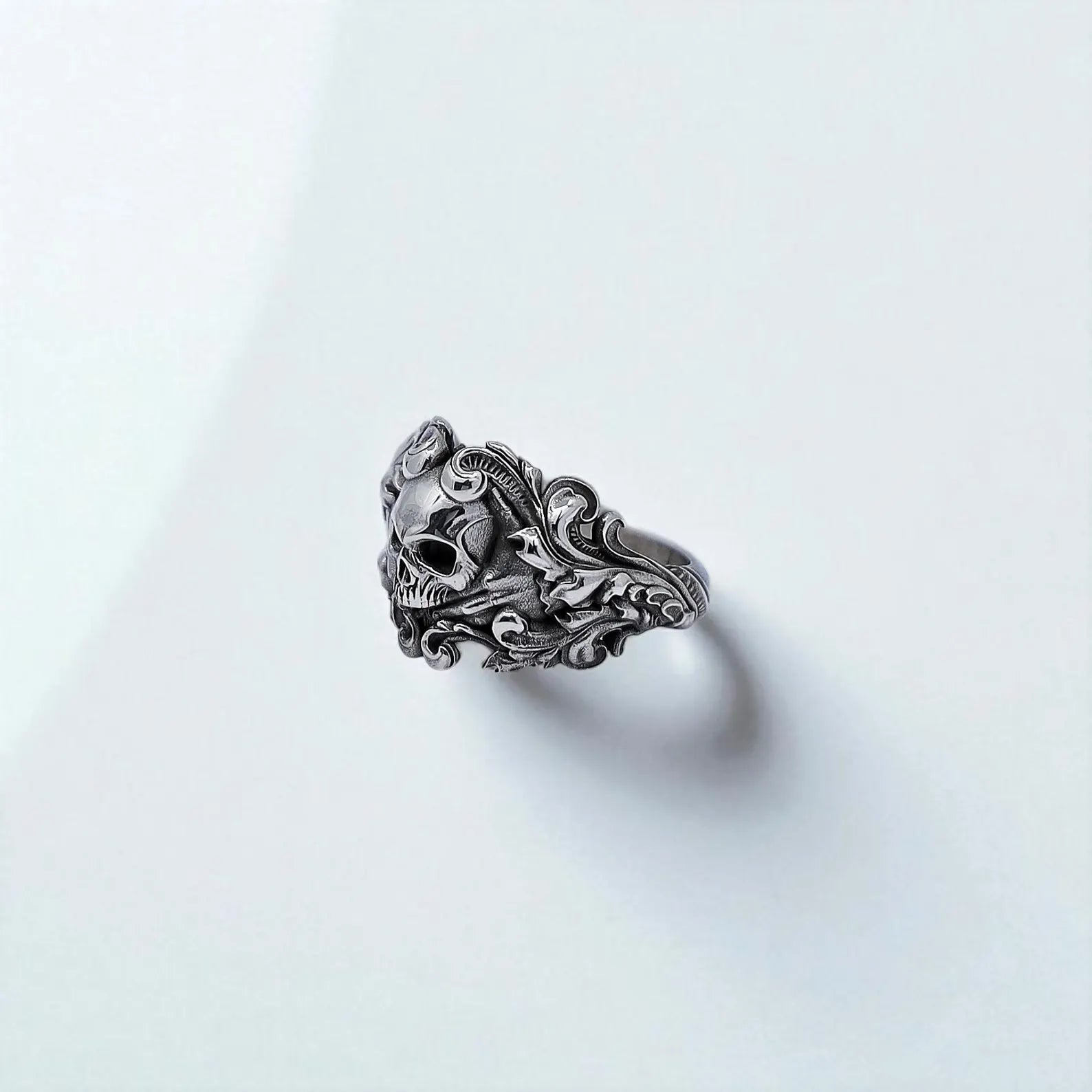 Close-up view of a silver skull ring with a fierce skeletal centerpiece and swirling gothic details, symbolizing rebellion, power, and mystery. Perfect for those who embrace dark, edgy fashion.