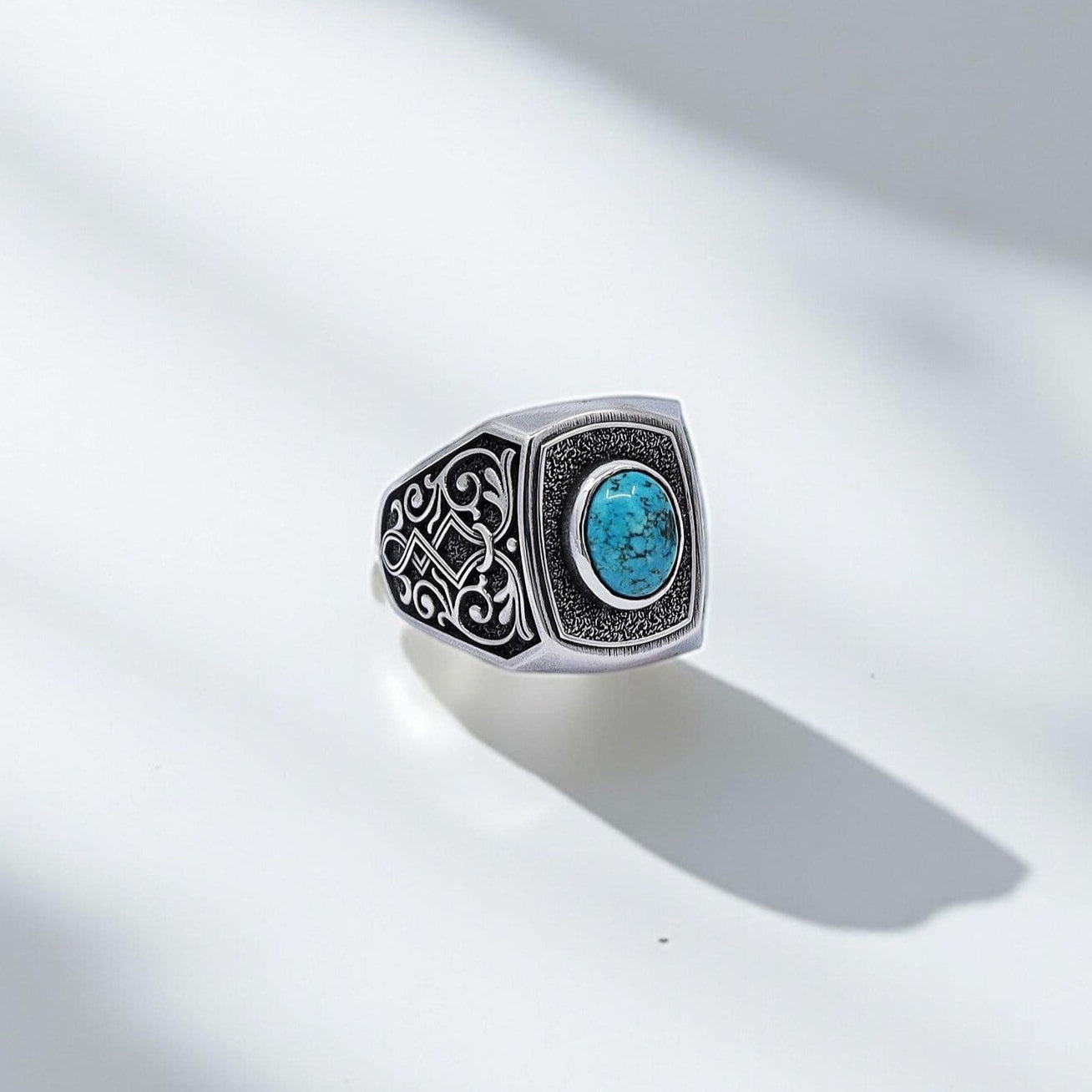 Close-up shot of a handcrafted sterling silver men's ring featuring a natural turquoise stone and intricate tribal patterns on each side, blending gothic and ethnic styles in a bold and unique design.