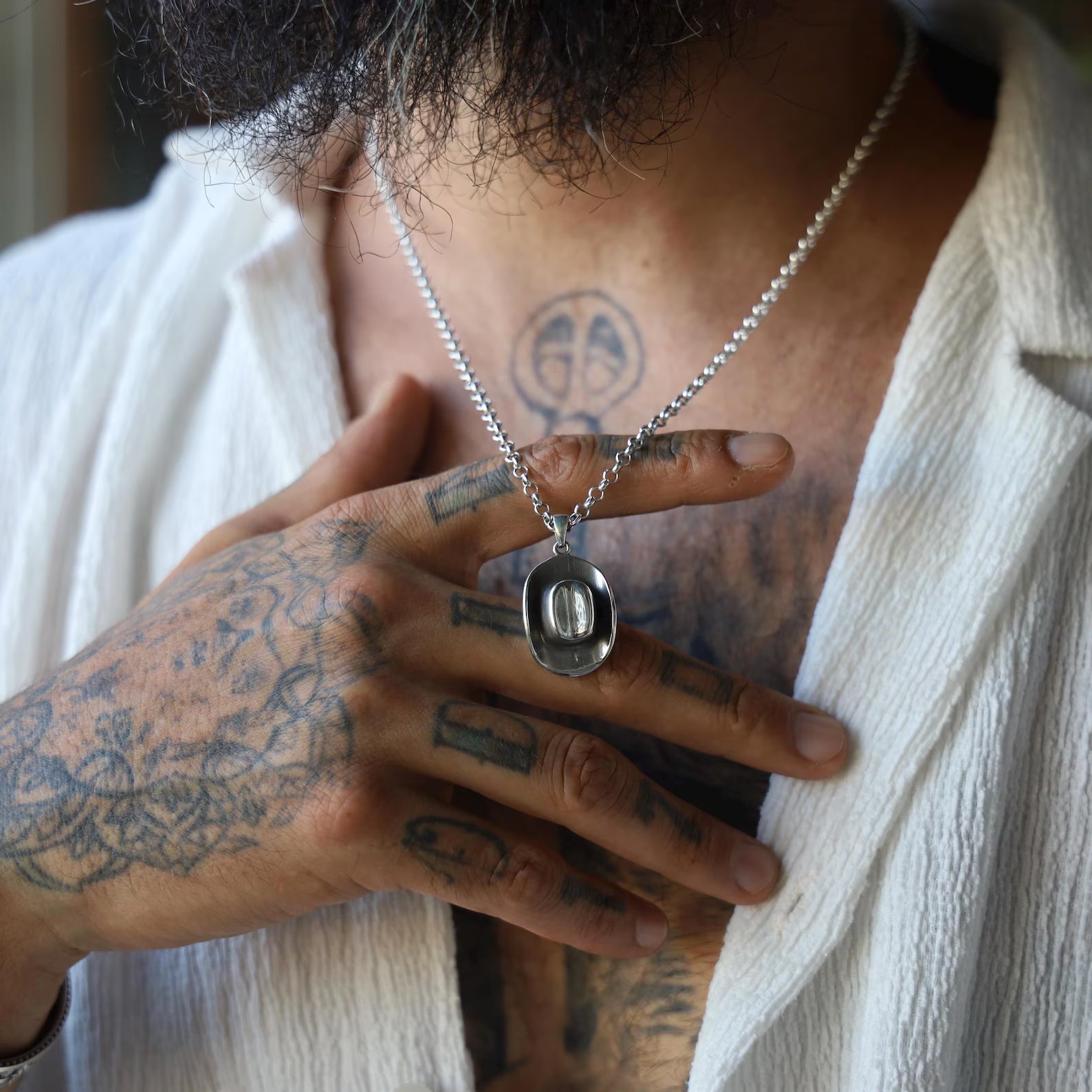 Artisan cowboy necklace showcasing a solid silver pendant shaped like a classic western hat, reflecting rugged charm and timeless cowboy style, photographed with natural lighting on a reflective surface.