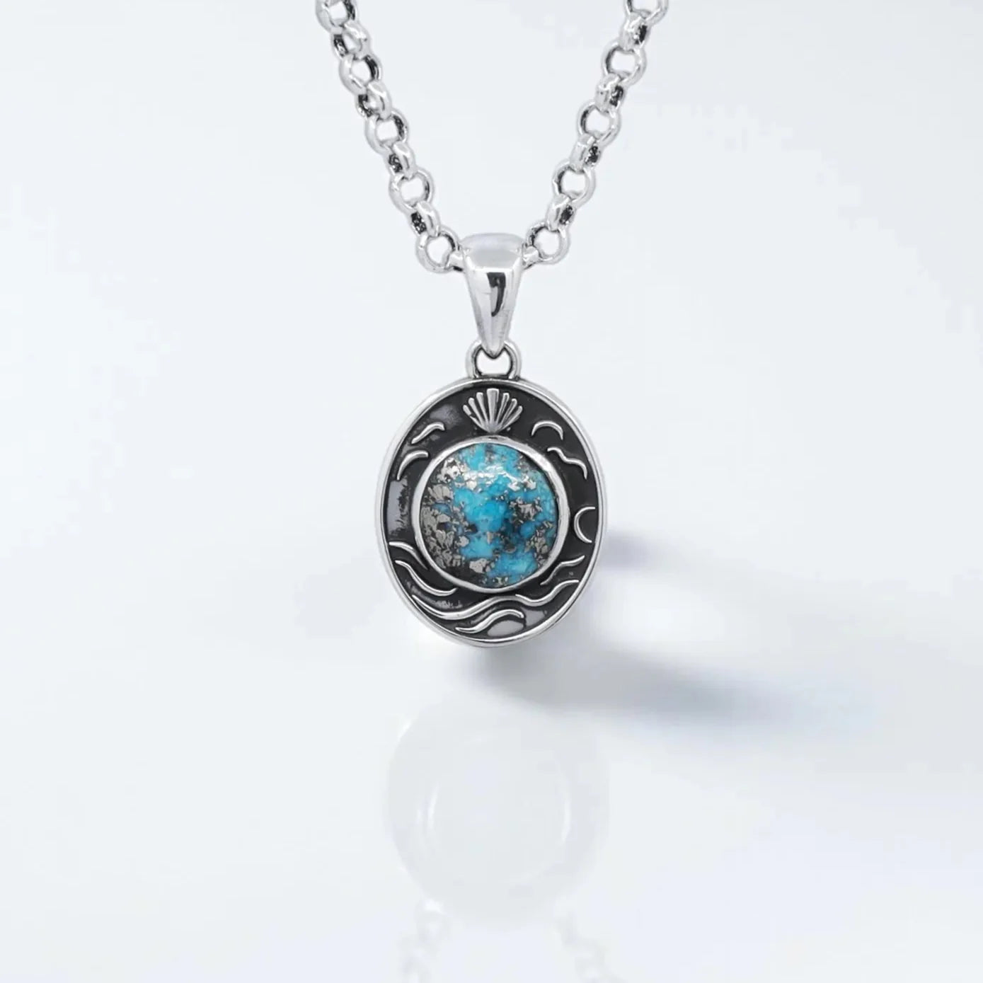Close-up image of a handcrafted sterling silver pendant necklace featuring a natural turquoise gemstone in the center, surrounded by detailed ocean wave and seashell engravings, reflecting nautical elegance and artisan craftsmanship