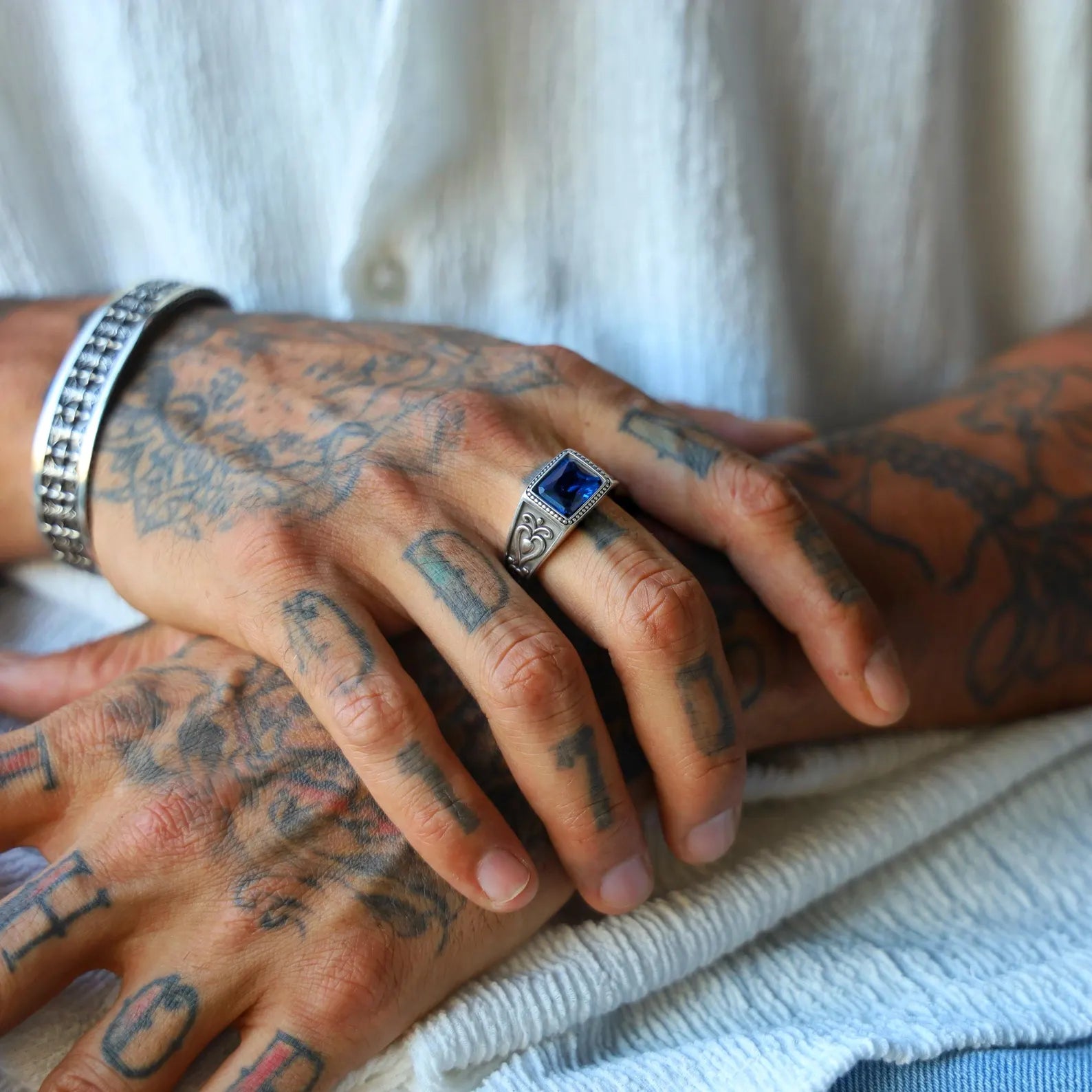 Close-up image of a handcrafted sterling silver men's ring featuring an emerald-cut sapphire blue gemstone with gothic detailing, designed as a bold and timeless gift for him.