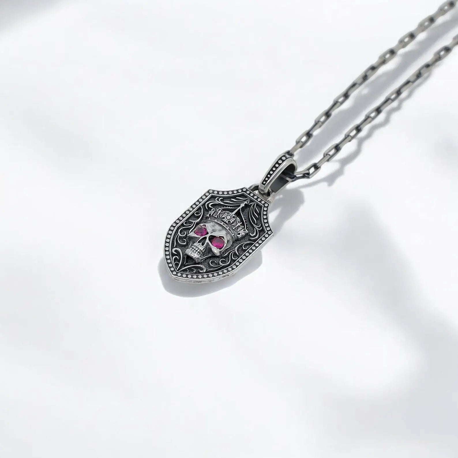 Sterling silver skull sword necklace with double-sided pendant design, featuring a crowned skull with red gemstone eyes on one side and a detailed sword engraving on the other. This handcrafted gothic shield necklace blends medieval warrior vibes with dark elegance, making it perfect for fans of Days Gone, punk fashion, and skull jewelry.