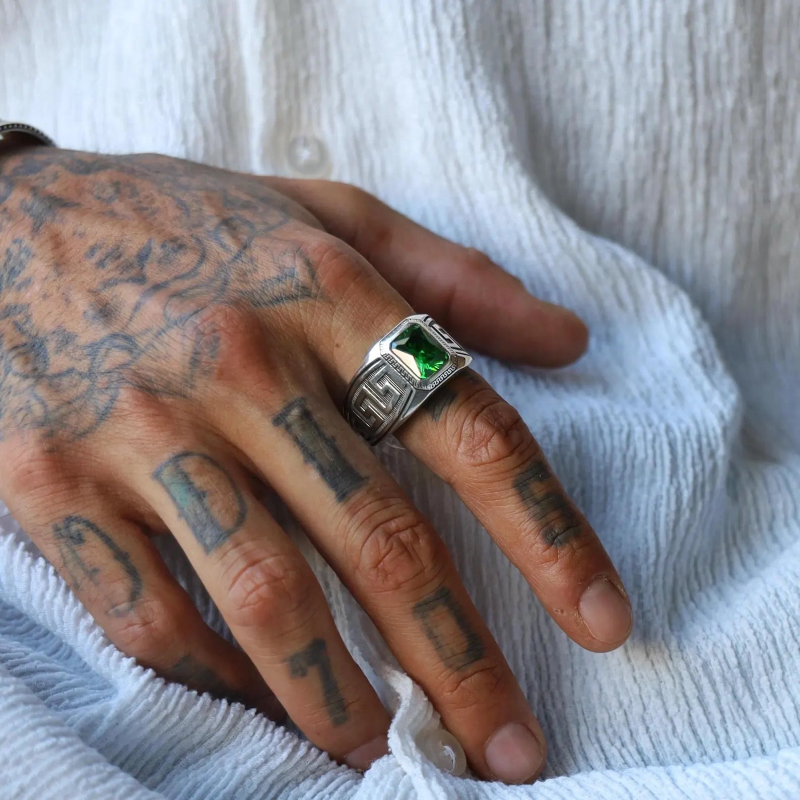 Close-up image of a handcrafted sterling silver Greek ornament ring for men, featuring an emerald-cut green gemstone in the center, surrounded by detailed Hellenic patterns that reflect ancient aesthetics and timeless elegance.