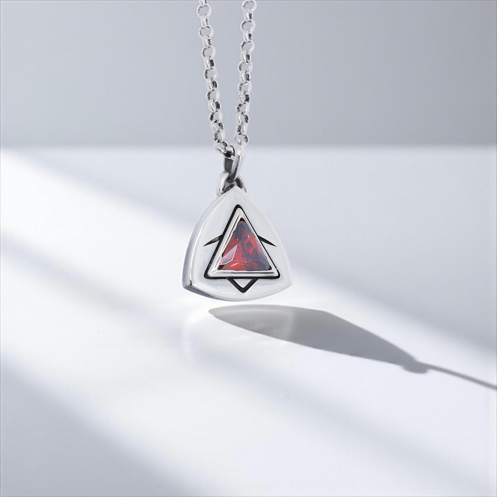 Detailed macro shot of a handcrafted geometric ruby necklace, emphasizing the high-quality triangular gemstone and precise silverwork, perfect for gothic, Viking, or cyberpunk-inspired fashion enthusiasts.