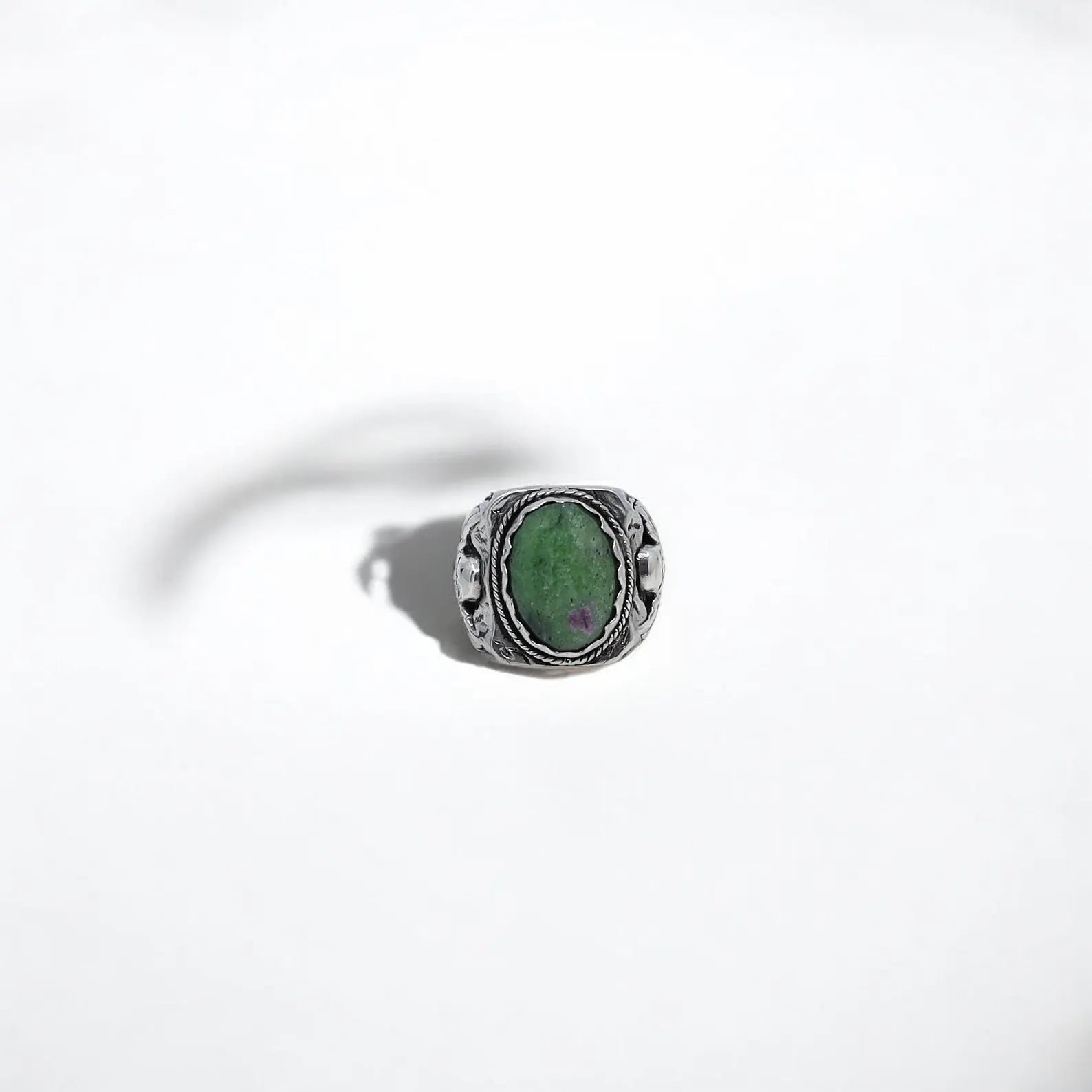 A unique silver ring featuring an oval-shaped green ruby zoisite gemstone securely set atop a band engraved with skull designs, crafted by hand with exceptional precision. This ring embodies raw attitude and symbolic strength, making it a meaningful piece for those who appreciate edgy, gothic jewelry. Perfect as a gift for men on anniversaries, birthdays, or as a custom-engraved keepsake.