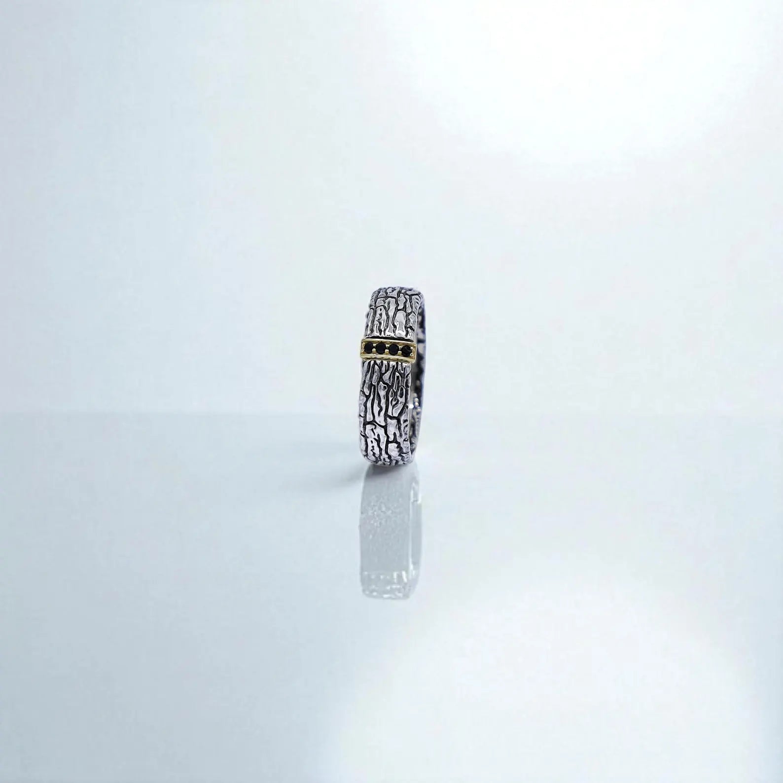 Close-up diagonal view capturing the handcrafted silver band with raw carved textures, gold accent overlay, and embedded dark stones. This unique ring speaks to strength, style, and individuality — ideal for modern men who appreciate edgy fine jewelry.