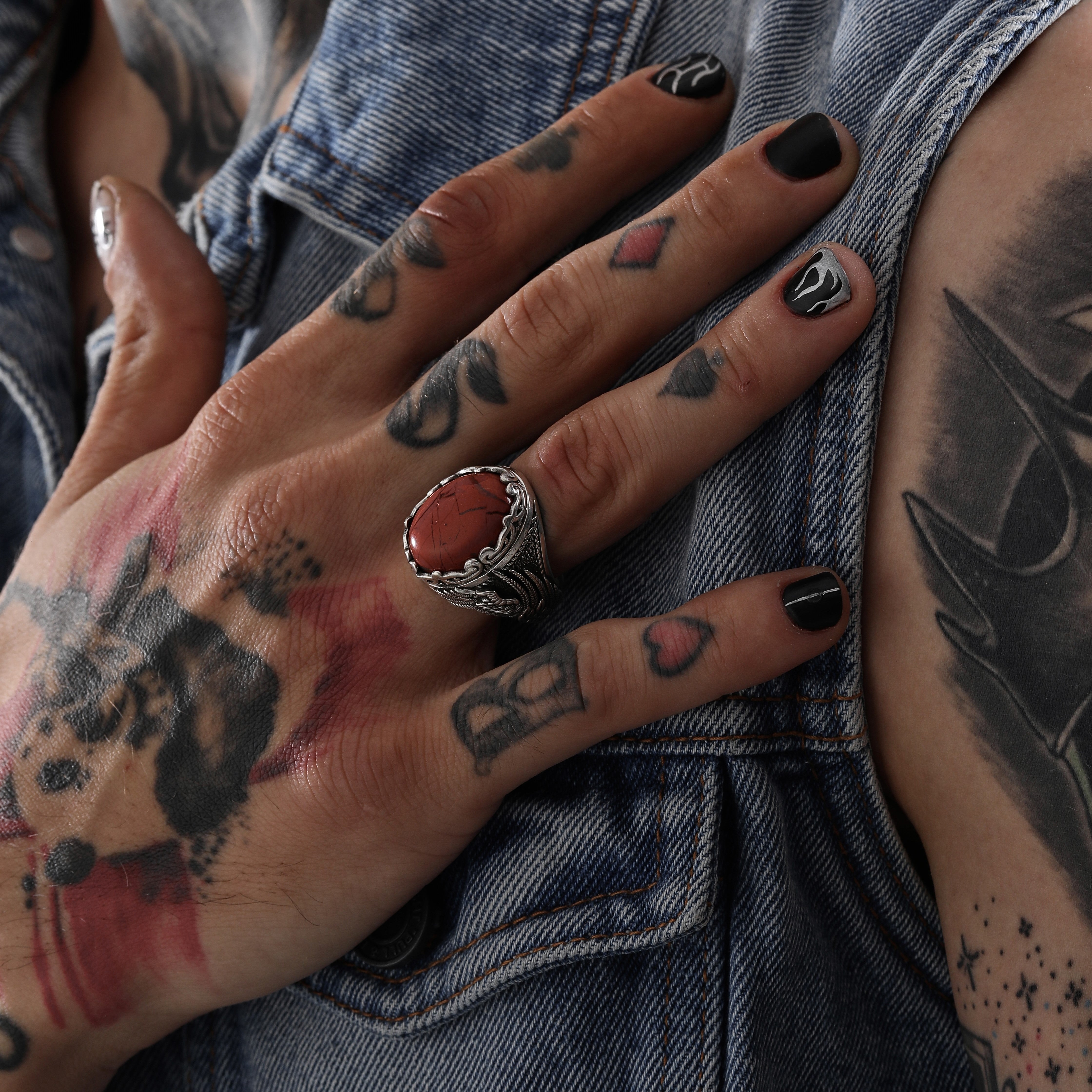 A deeply symbolic statement ring made of solid sterling silver, featuring an oval-cut red jasper stone known for its grounding energy and natural beauty. The handcrafted detailing on the band resembles wings or flame patterns, reflecting themes of transformation and strength. This gothic-inspired ring is made for those who express themselves through bold accessories and appreciate handmade silverwork.