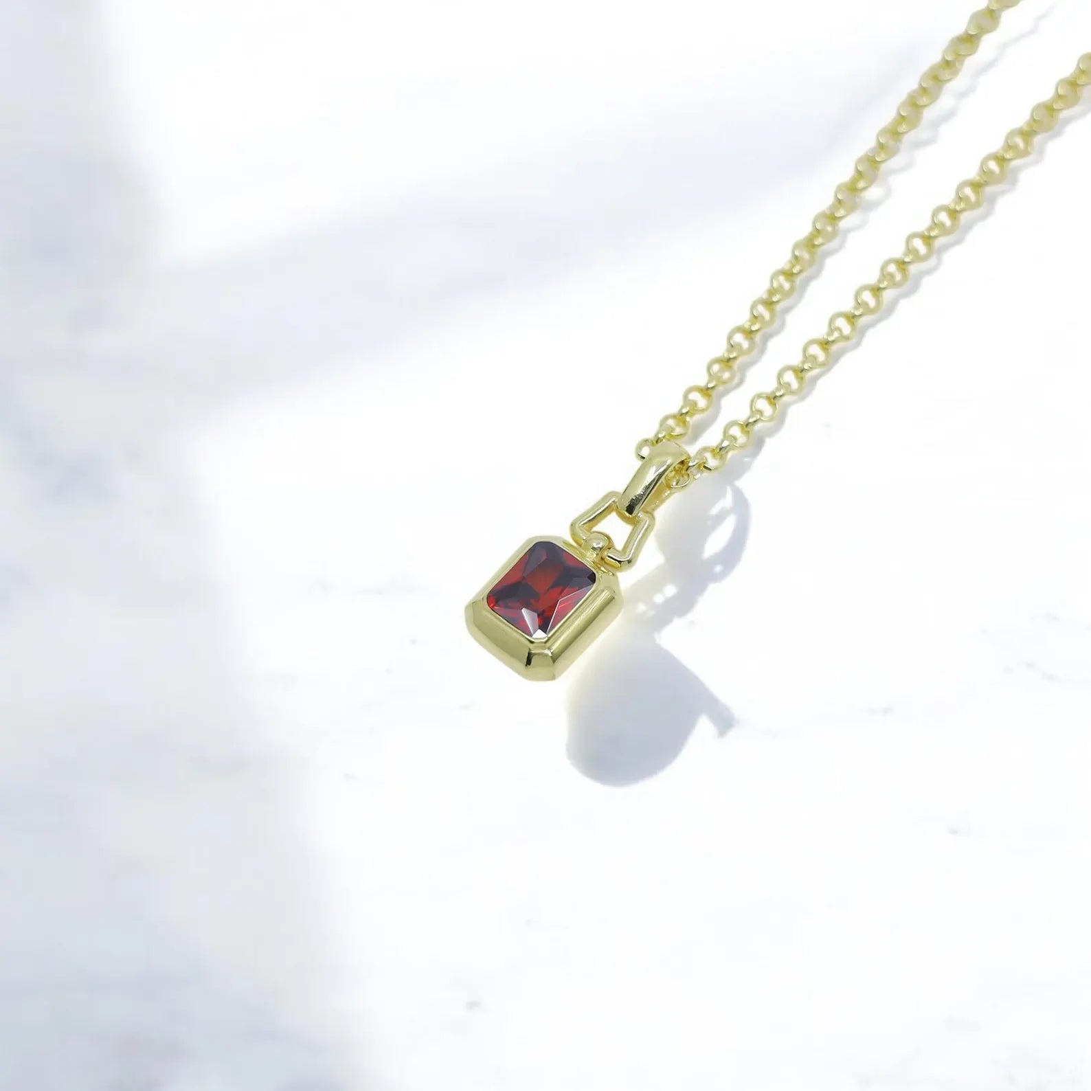 Close-up of emerald cut lab ruby gemstone pendant in 14K gold plated silver, showcasing the brilliance of the red stone. A handcrafted, unisex necklace that combines sophistication with timeless charm, perfect for jewelry lovers looking for a luxurious gift idea.