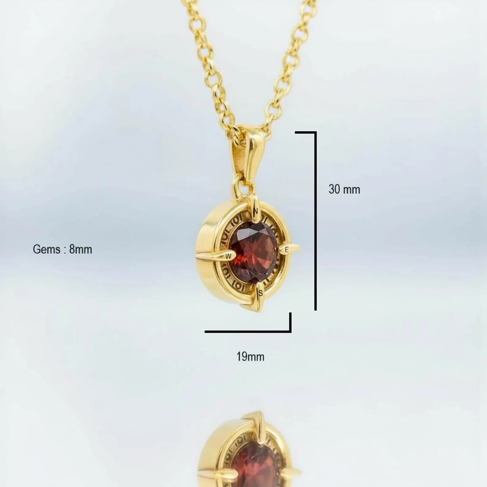 Close-up of gold plated compass pendant featuring deep red garnet, symbolic exploration and guidance jewelry.