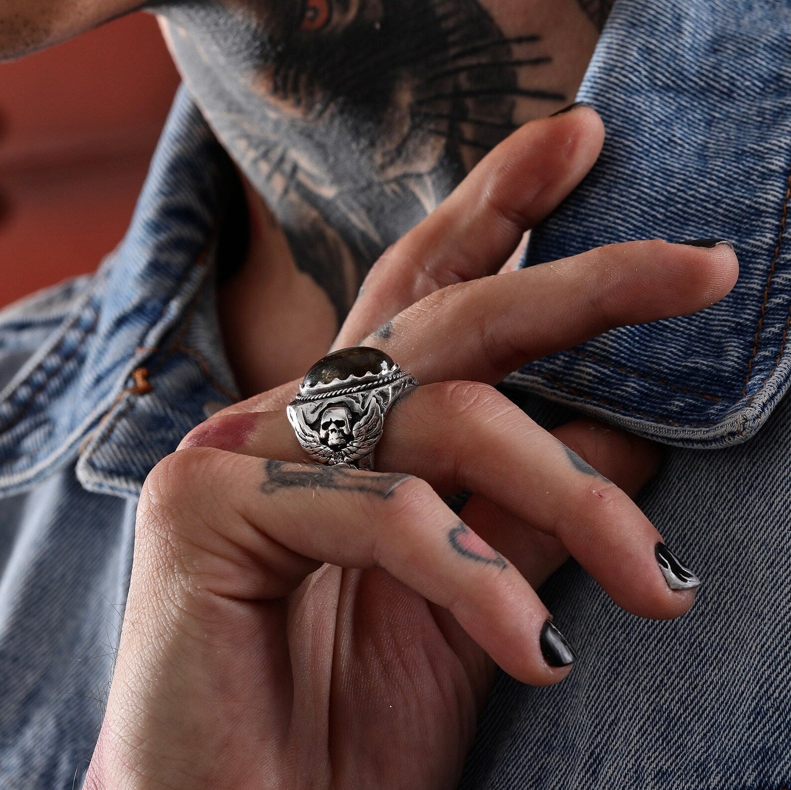 A heavy-duty sterling silver ring designed with a natural labradorite gemstone and gothic skull carvings, perfect for motorcycle enthusiasts and alternative fashion lovers. The handcrafted detailing adds depth and personality to this statement mens ring.