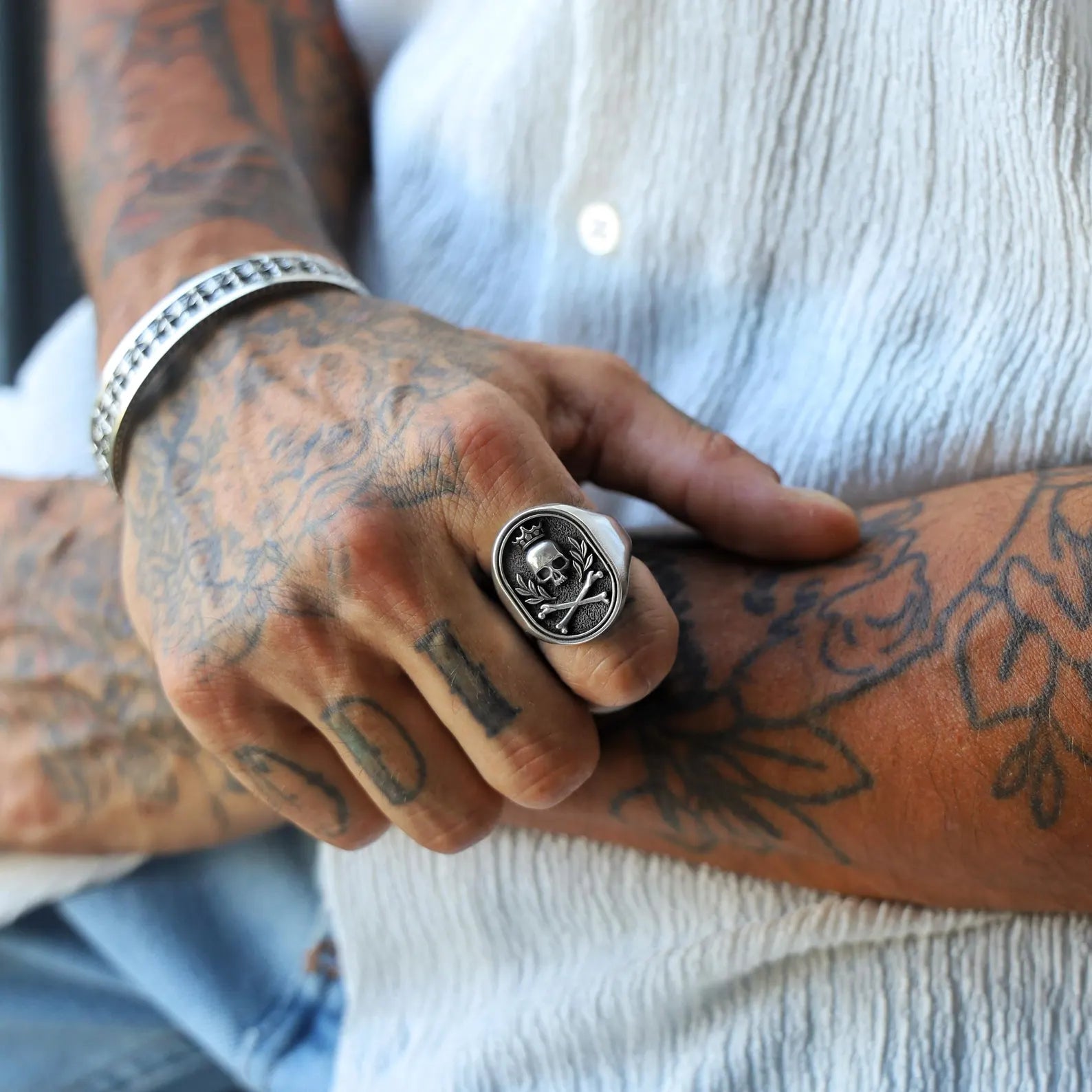 Sterling silver men's signet ring showcasing an intricately carved crowned skull with crossbones, blending gothic aesthetics with rugged biker fashion, ideal for those who appreciate powerful and edgy jewelry.