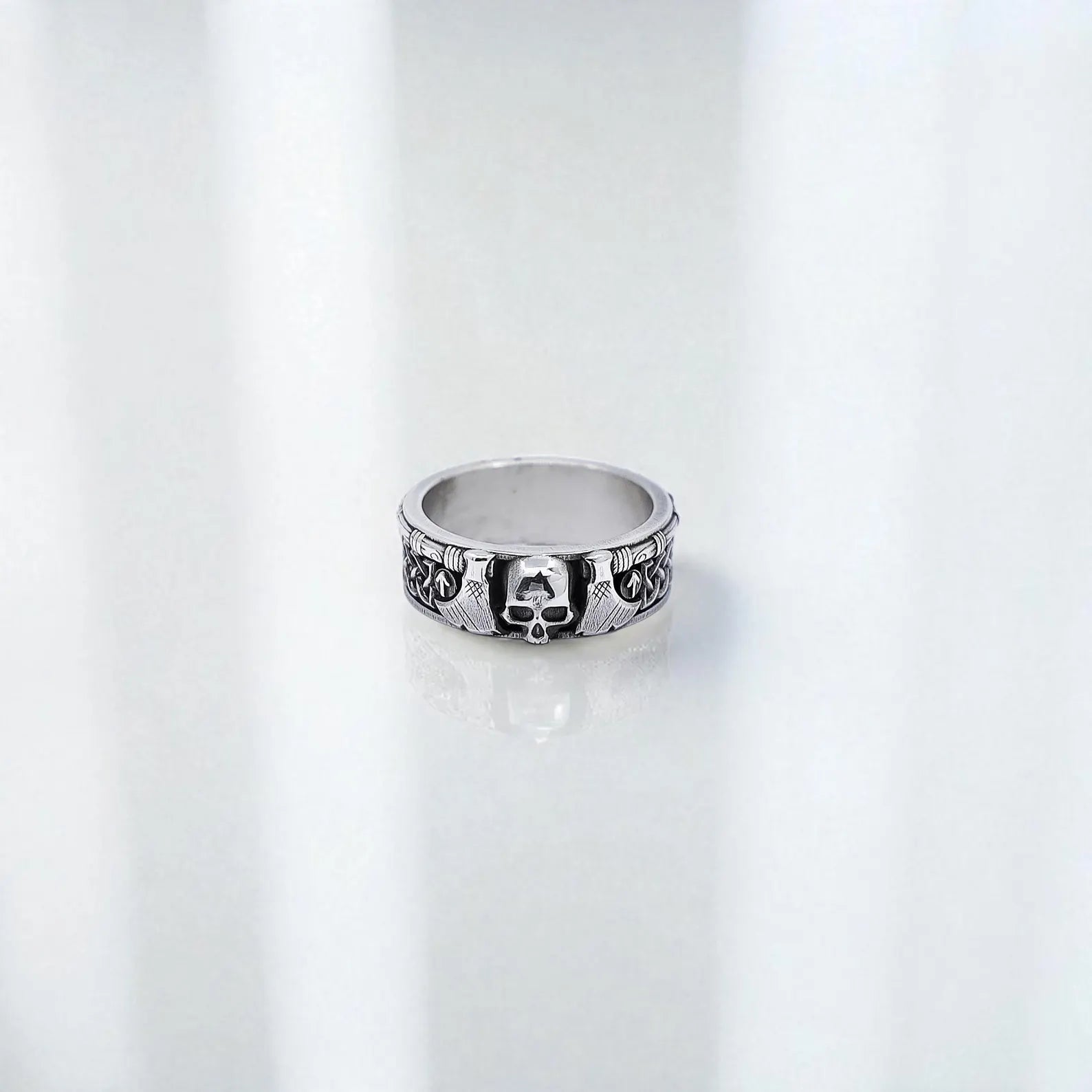 Masculine Viking skull ring displayed on a reflective surface, symbolizing ancient Nordic power and warrior energy. Made with solid sterling silver and engraved with axes and sacred knotwork. Ideal gift for men who appreciate gothic jewelry, Norse heritage, or handcrafted artisan rings with a deep symbolic meaning.
