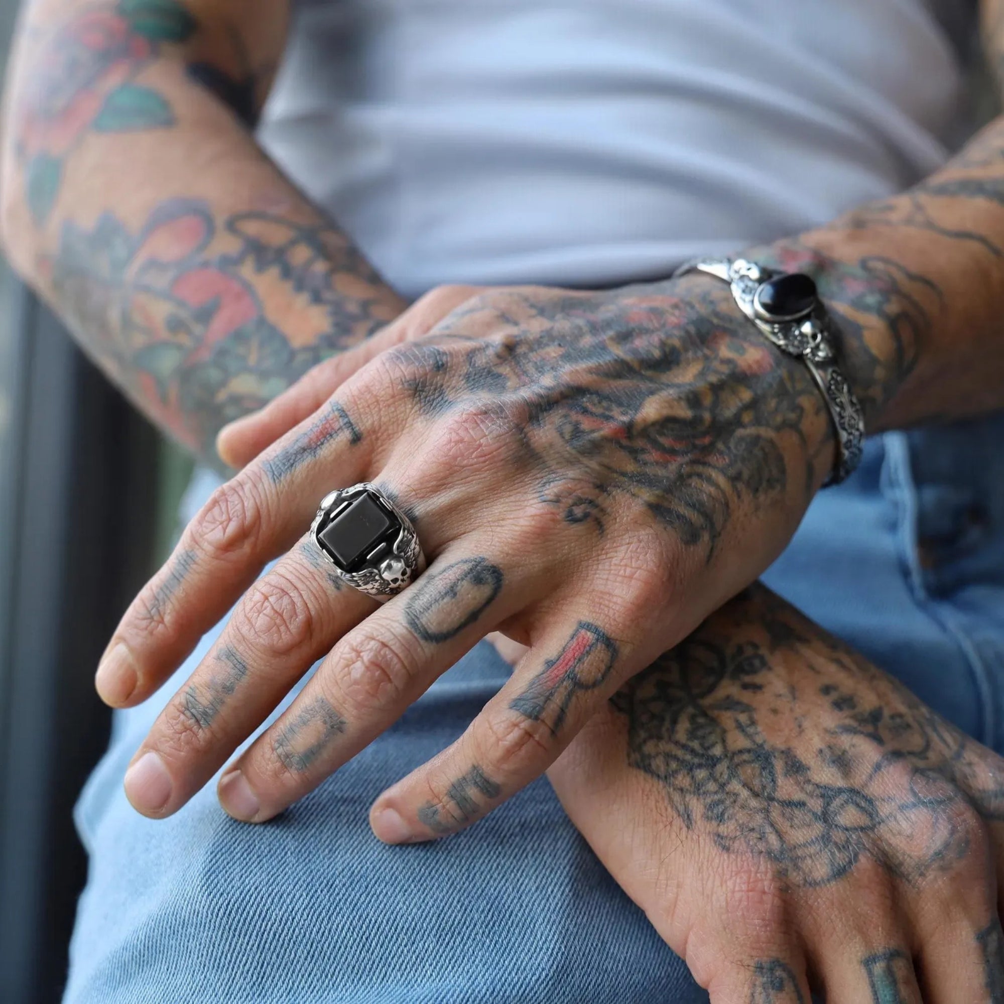 Luxury close-up of a gothic silver bracelet for men with black onyx stone and twin skull engravings. This unique handmade design captures the essence of rebellion and strength, perfect for vintage and biker fashion enthusiasts.