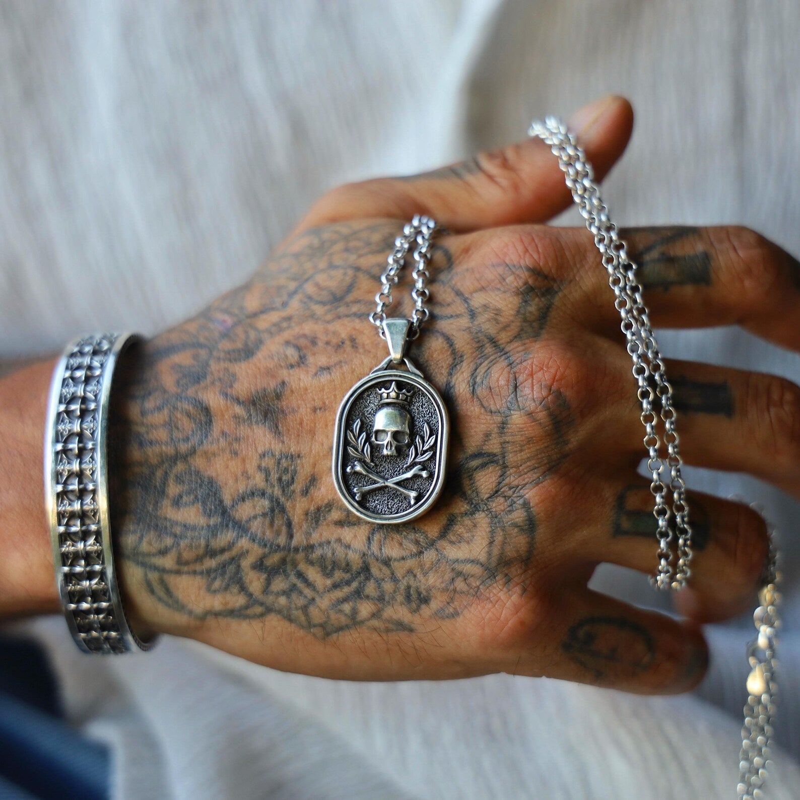 Sterling silver skull pendant with crossbones and laurel detailing, handcrafted for men who appreciate dark, symbolic jewelry with a punk rock twist; a unique gift for anniversaries or special occasions.