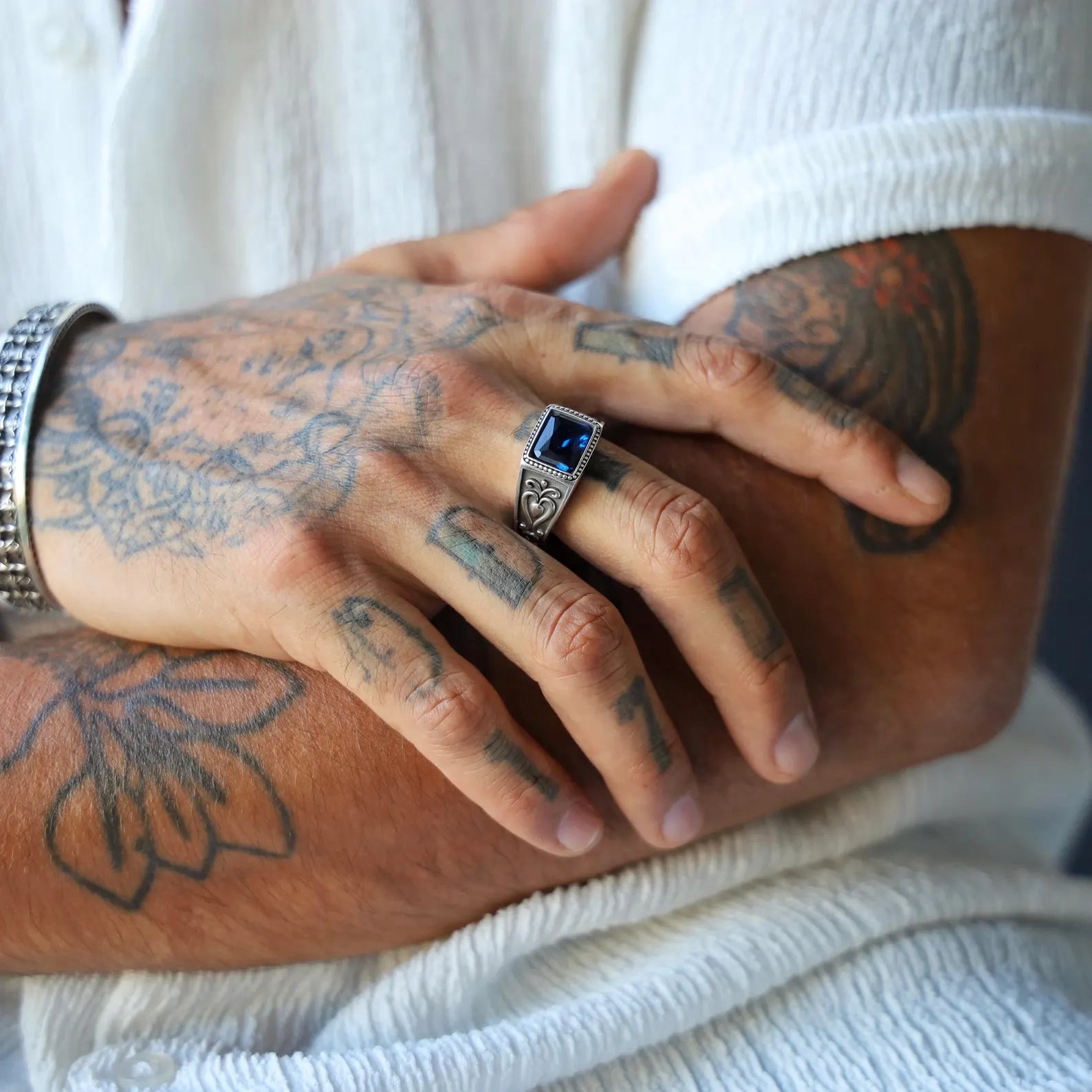 Detailed product photo of a men's emerald-cut sapphire blue ring with handcrafted silver scrollwork and customizable engraving option – ideal for biker, medieval, or gothic fashion lovers.