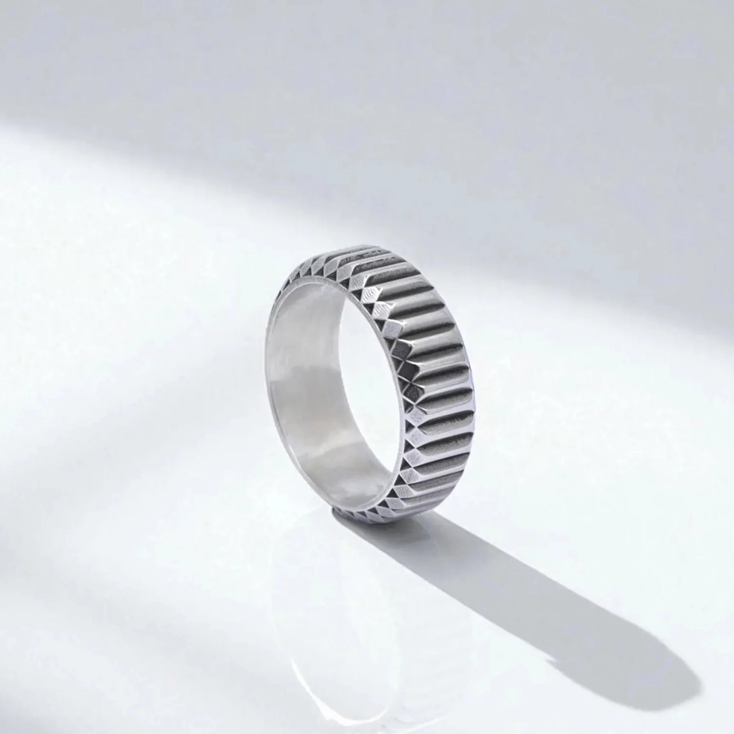 Sterling silver textured band ring for men featuring a bold geometric pattern and minimalist design, displayed on a clean white background with soft reflections. This handcrafted ring combines modern elegance with artisanal detail, ideal for fashion-forward men who appreciate sleek, structured jewelry.