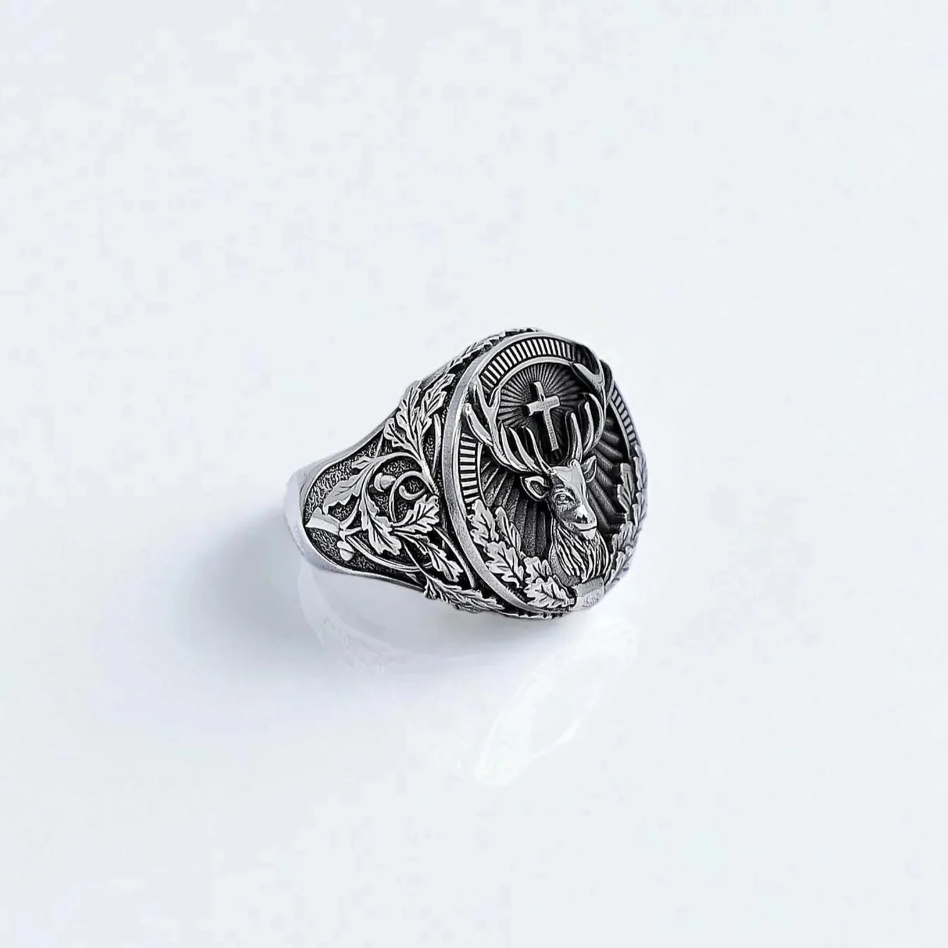 A handcrafted sterling silver ring featuring a detailed stag with a cross between its antlers, surrounded by gothic leaf engravings. The intricate front-facing design symbolizes strength, nature, and spiritual guidance, making it an ideal piece for outdoorsmen and lovers of symbolic jewelry.