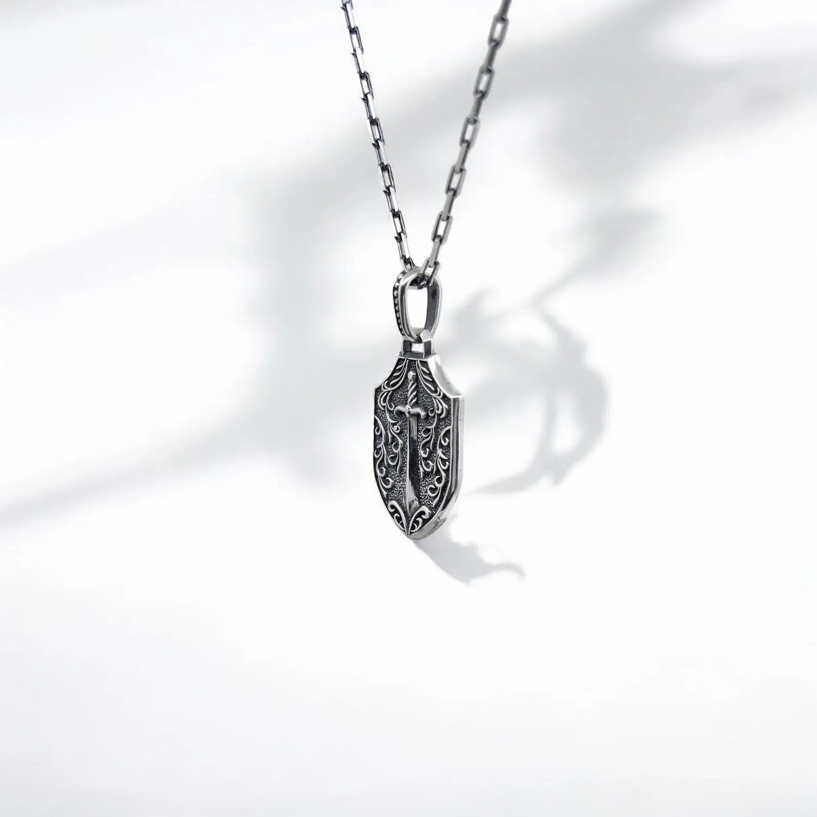 Warrior-inspired shield pendant necklace made of sterling silver, featuring a dual-face design: a crowned skull with blood-red eyes and a sword on the reverse. A gothic, punk-style accessory perfect for those who embrace individuality, rebellion, and meaningful handmade jewelry.