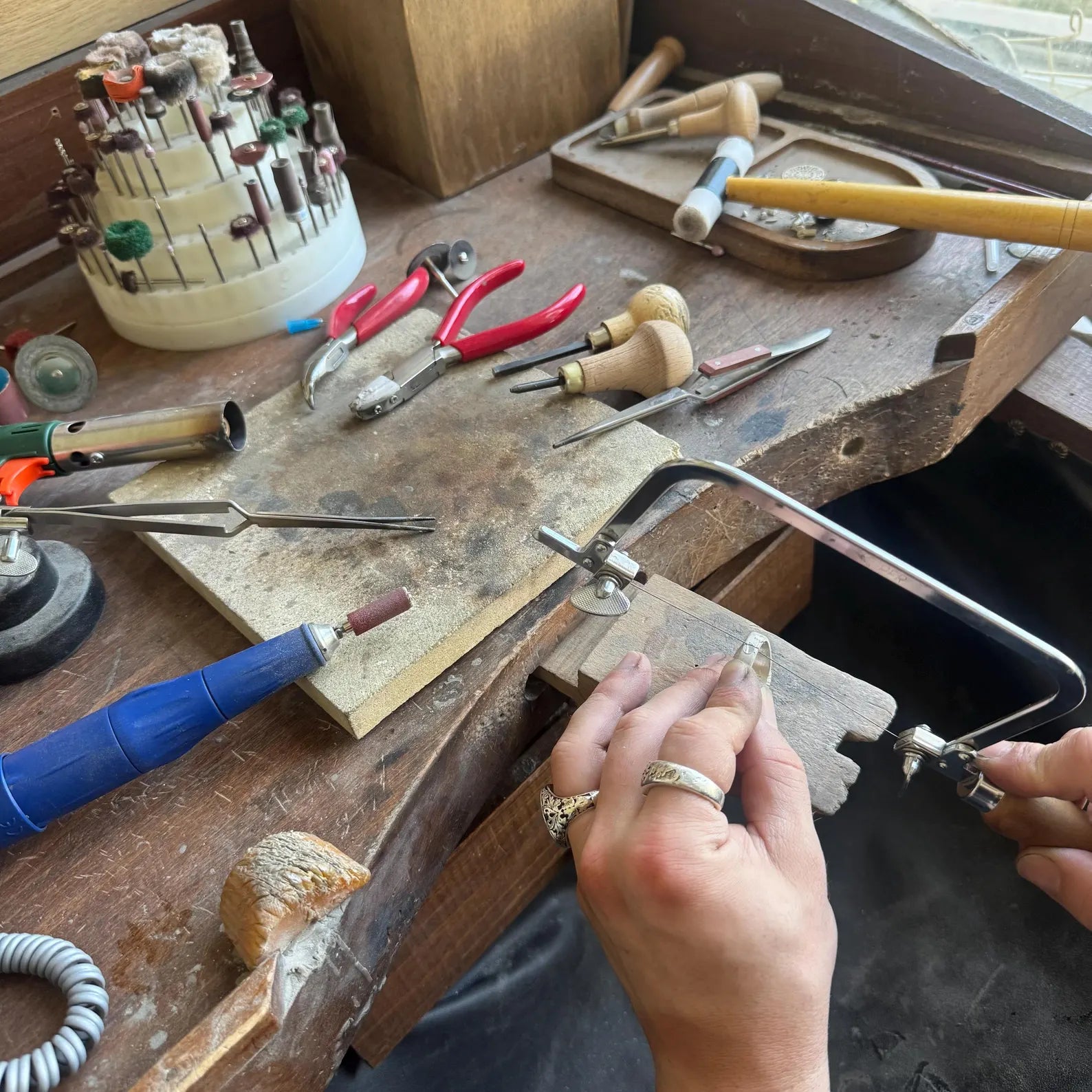 Jewelry-making process on a workbench with tools and hands working.