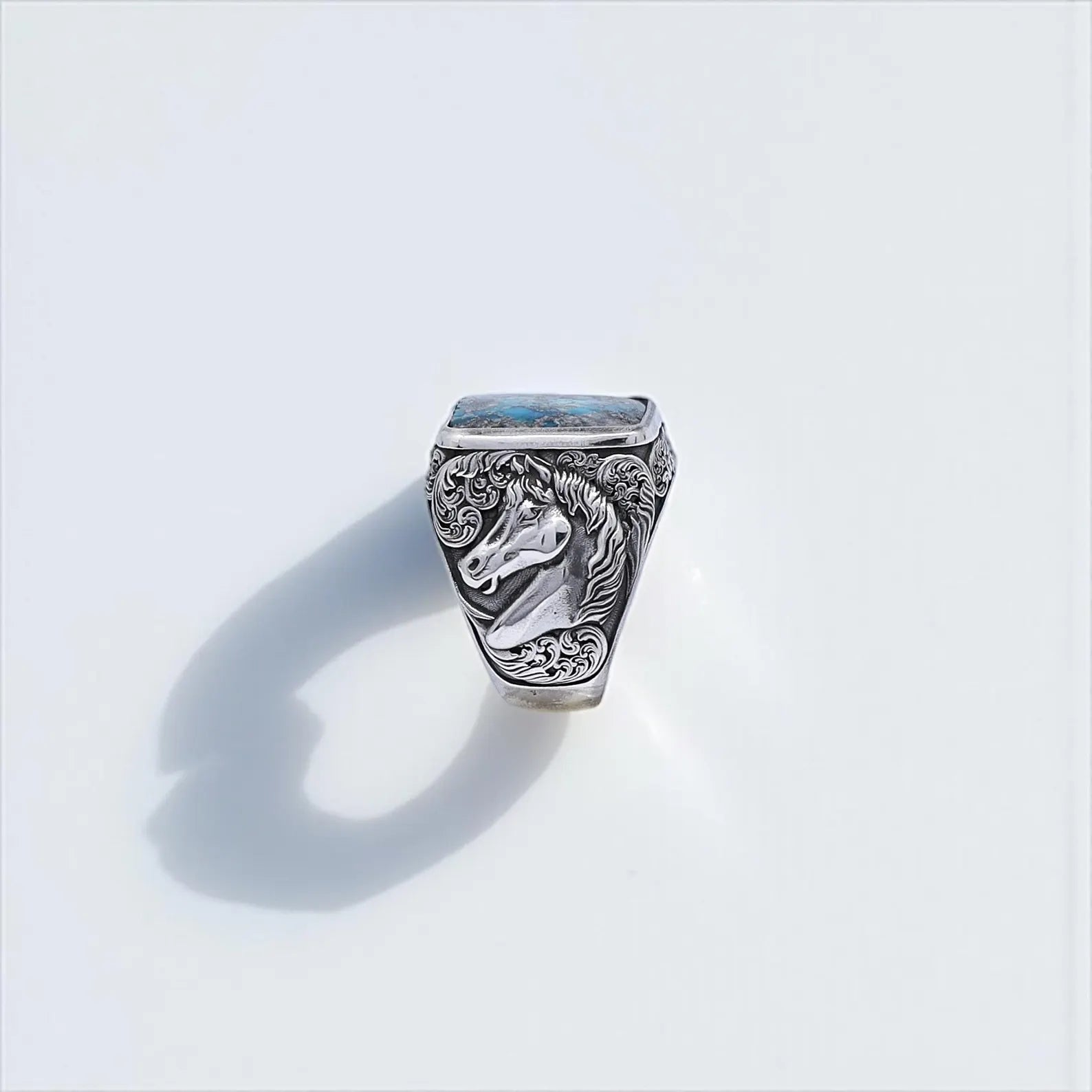 Western-inspired handcrafted men’s ring made of solid sterling silver, featuring a square turquoise gemstone centerpiece with detailed textures. The ring is accented with engraved horse head designs on both sides, blending cowboy aesthetics with artisan craftsmanship. Ideal for southwestern jewelry lovers and bold masculine style.