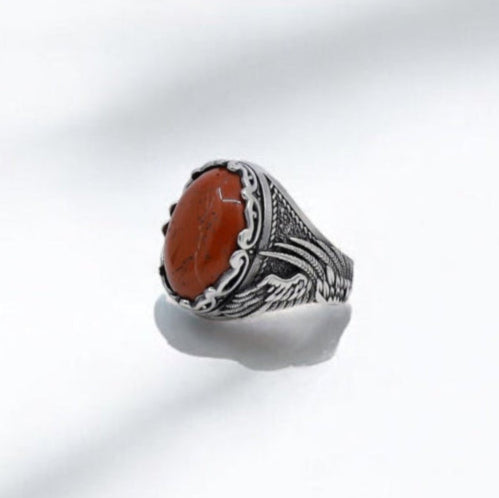 A handcrafted sterling silver ring for men featuring a genuine red jasper gemstone and ornate gothic engraving that wraps around the band in an elegant winged pattern. The deep red hue of the stone symbolizes energy and courage, making this bold ring a meaningful piece for men who embrace their strength and inner power. This statement accessory is perfect for bohemian souls, modern warriors, or anyone seeking a unique, nature-inspired ring that can also be engraved for a truly personal touch.