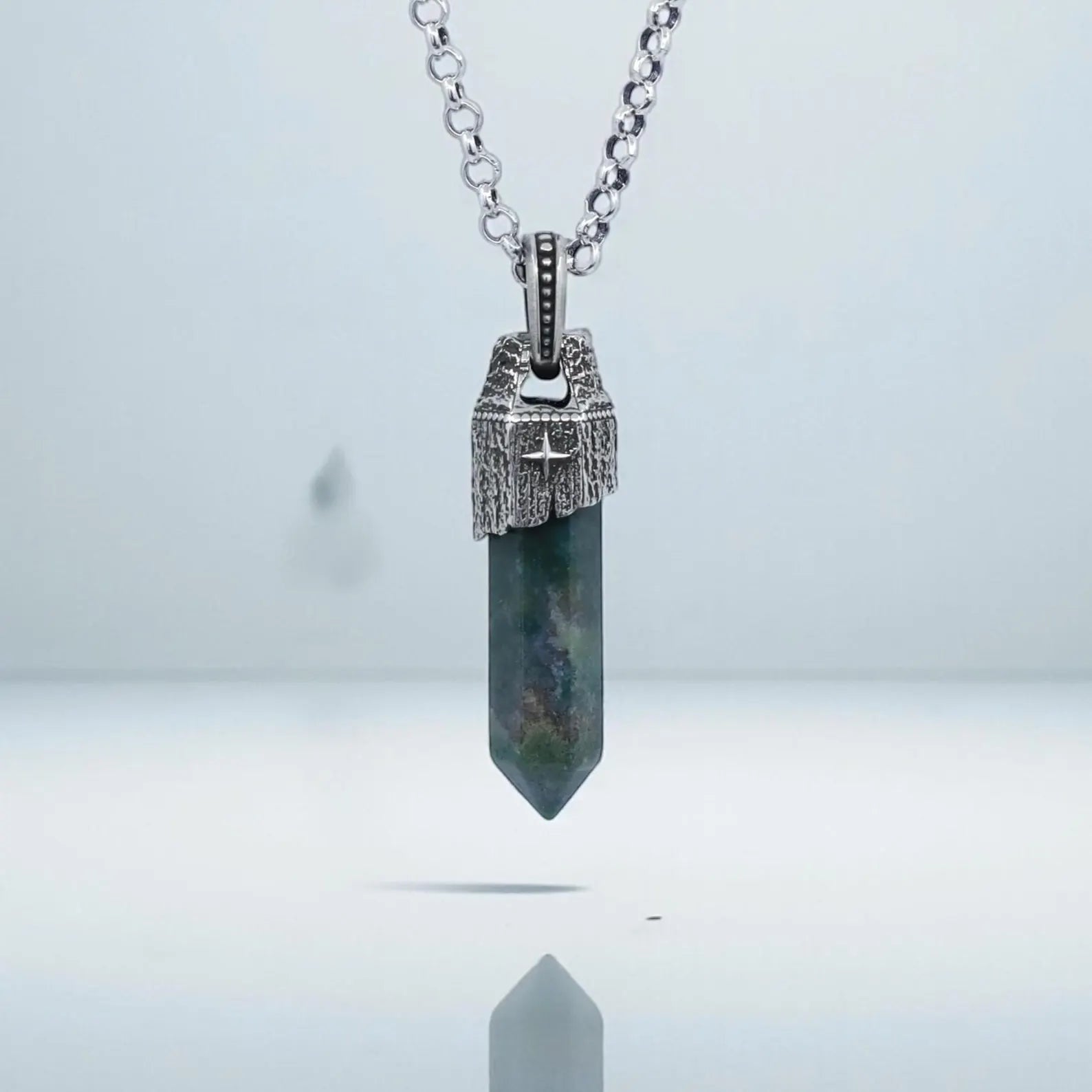 High-detail close-up of a handcrafted Moss Agate pendant necklace for men, featuring a natural green moss agate gemstone with earthy tones set in a vintage-style sterling silver compass frame, polished and oxidized for a bold nautical statement look.