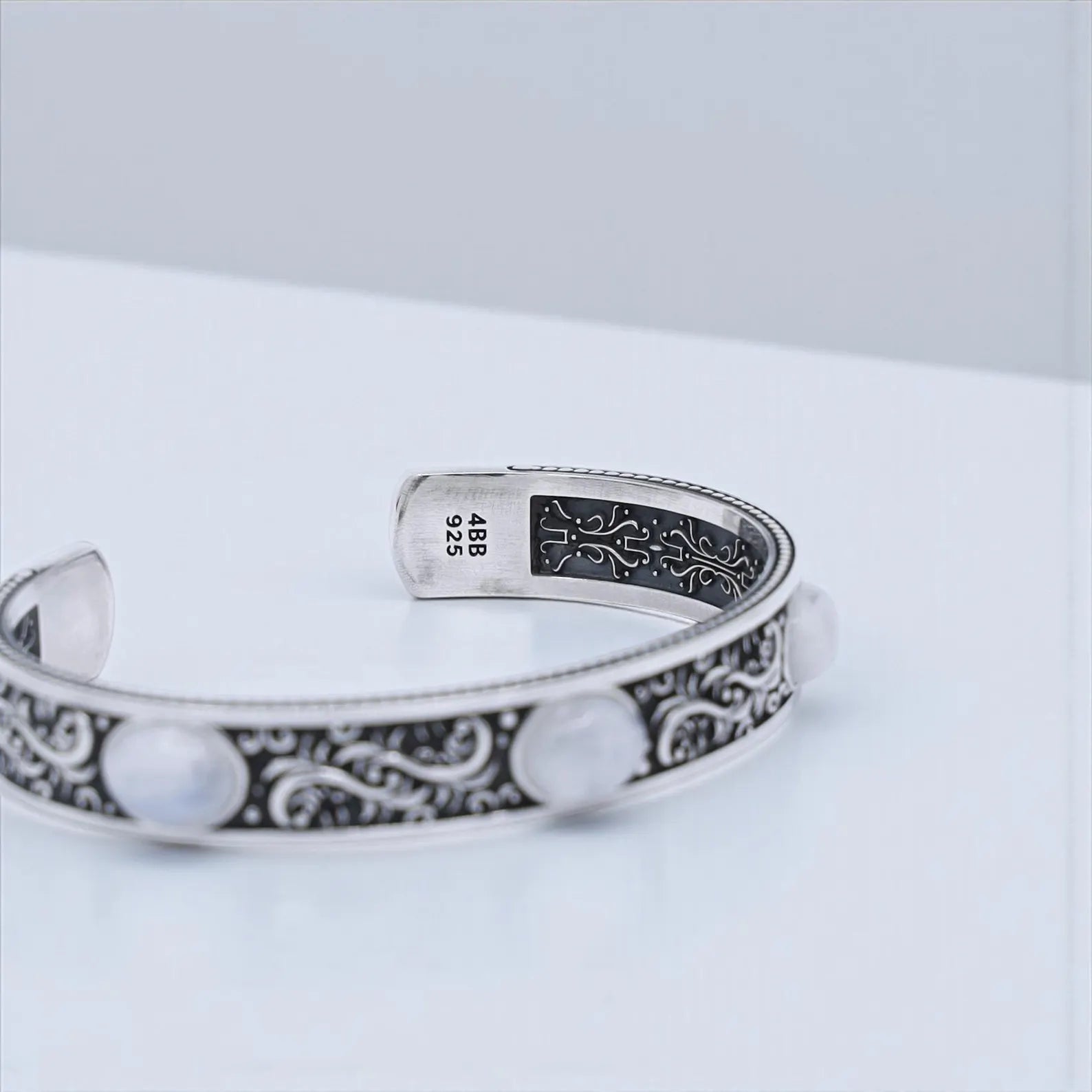 Handmade sterling silver cuff bracelet with moonstone centerpiece and side stones, designed with intricate Baroque-style scroll engravings. The perfect statement accessory or personalized gift for him.