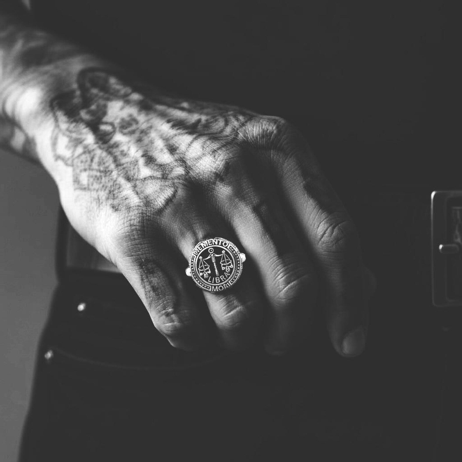 Detailed view of a Memento Mori Libra ring highlighting the skull and scale centerpiece, oxidized silver finish, and intricate handcrafted textures.
